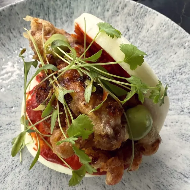 Pan bao relleno con hierbas frescas y salsa roja.