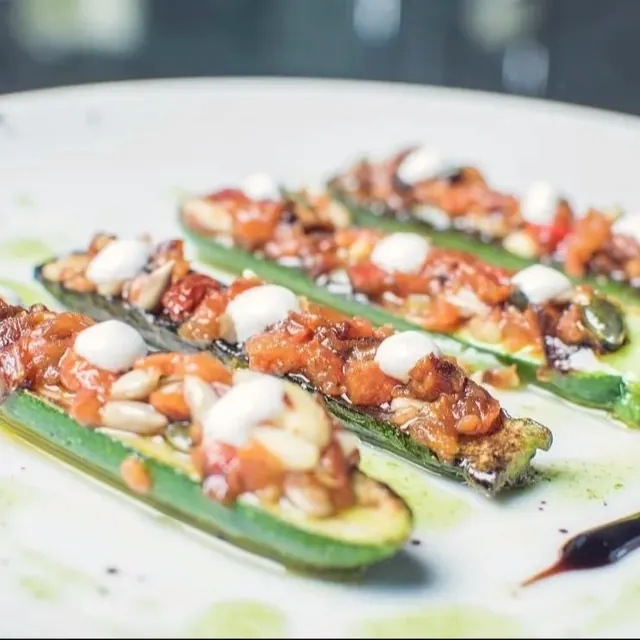 Calabacitas rellenas con verduras y piñones, en plato blanco.