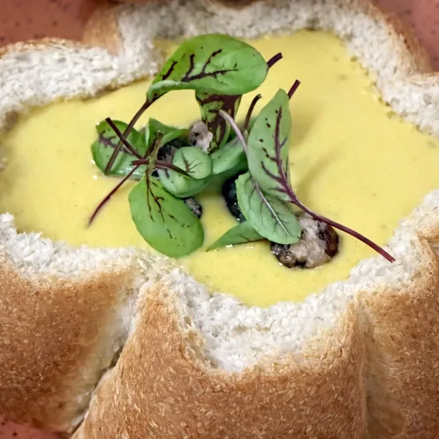 Crema servida dentro de un pan, con brotes verdes al centro.