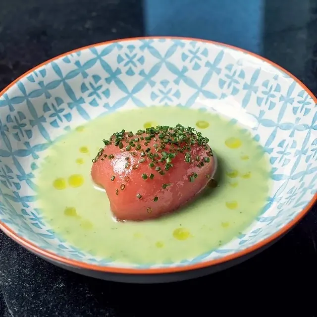 Jitomate pelado sobre una sopa verde con cebollín, en plato de cerámica azul.